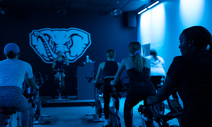 Group riding stationary bikes in light filled with blue light