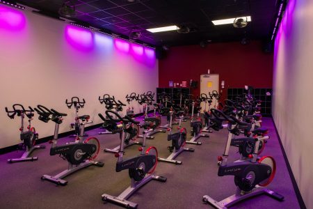 several bikes lined up inside the cycling studio illuminated by pink overhead lighting